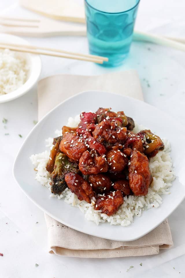 General Tso's Chicken plated over a bed of white rice with a blue drinking glass to the side.