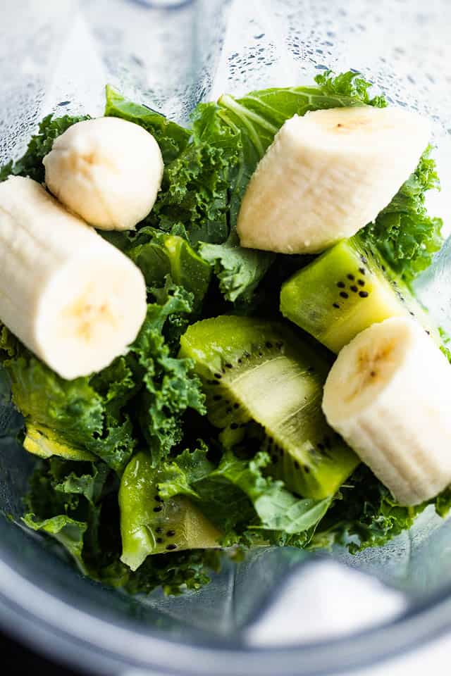 overhead shot of kale leaves, bananas, and kiwis in a blender.