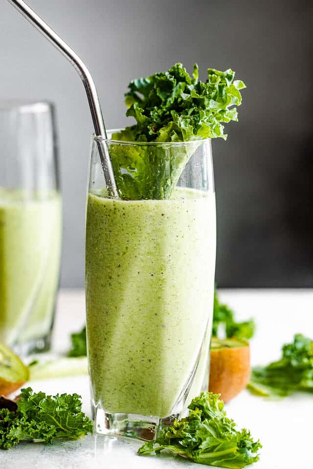 Side shot of two tall drinking glasses filled with green smoothies.