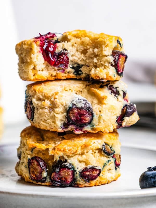 Three blueberry biscuits stacked on a plate with a bite missing from the top biscuit.