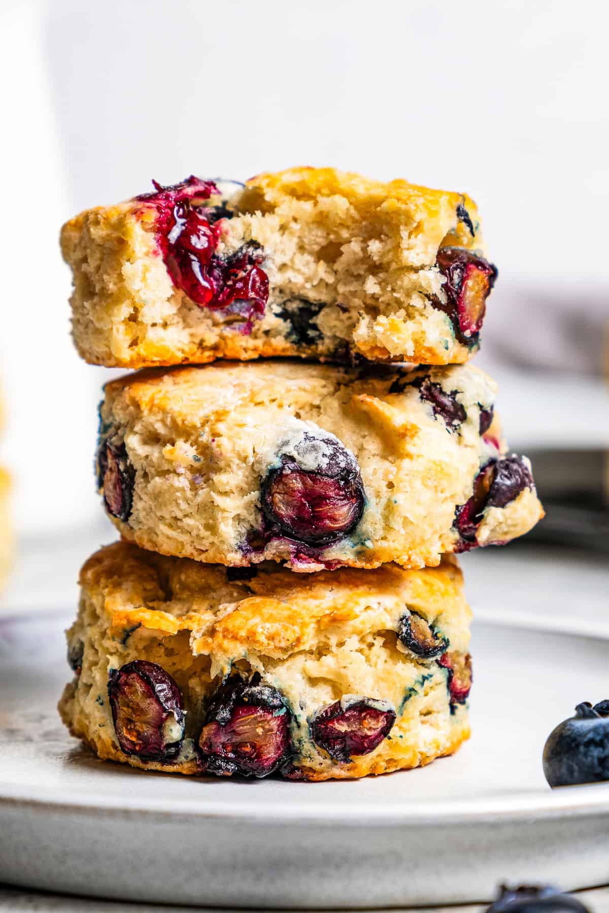 These easy blueberry biscuits are tender, buttery, and bursting with fresh blueberries! Enjoy them for breakfast, brunch, or as a snack. Three blueberry biscuits stacked on a plate with a bite missing from the top biscuit.