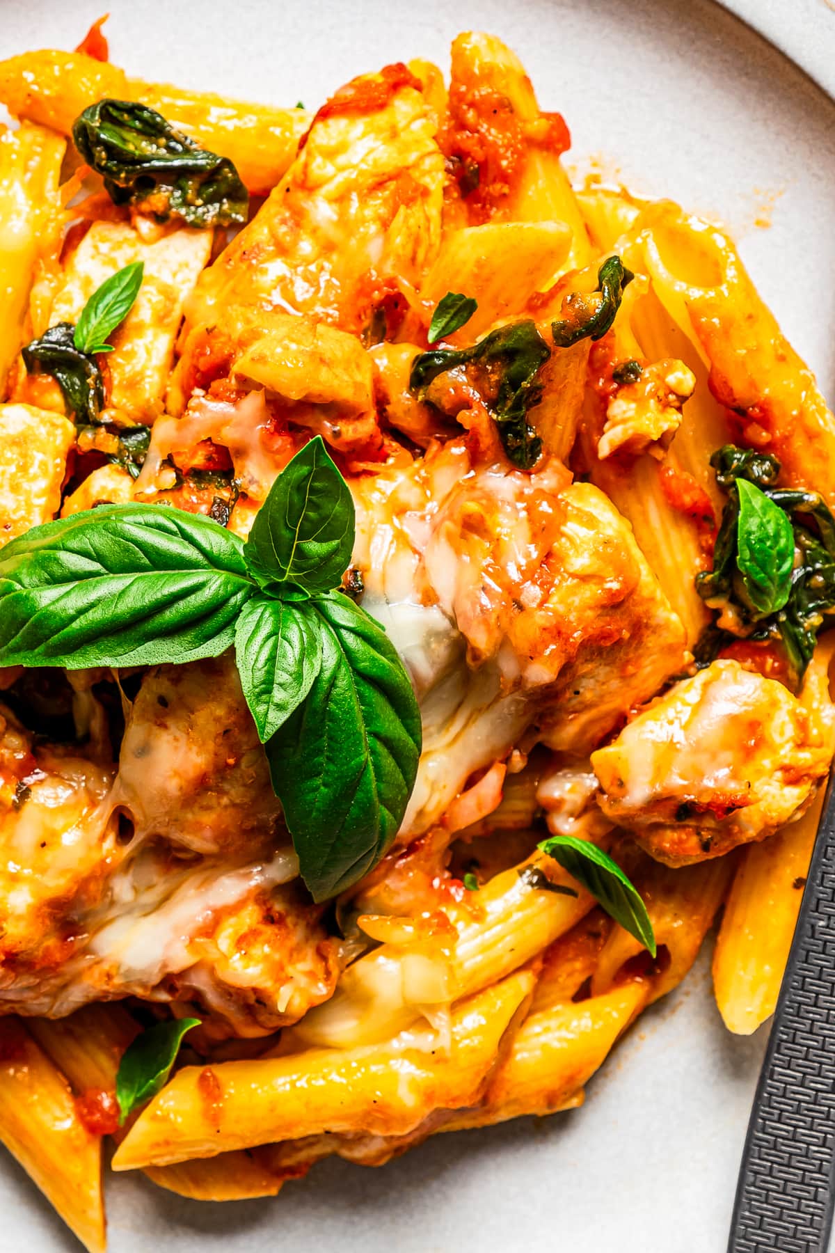 Close up overhead view of a serving of chicken pasta bake garnished with basil leaves on a plate.