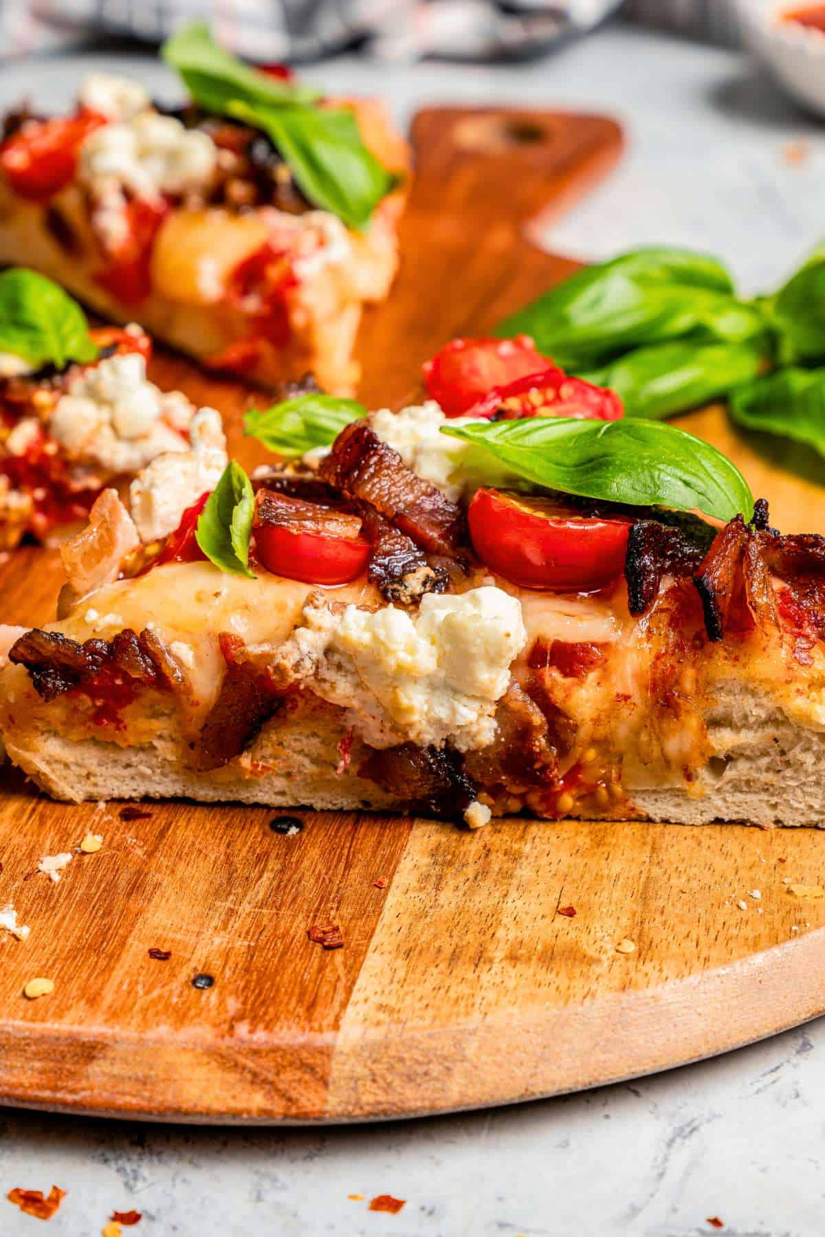 A slice of pizza topped with goat cheese, cherry tomatoes, and fresh basil leaves, and set on a wooden board.