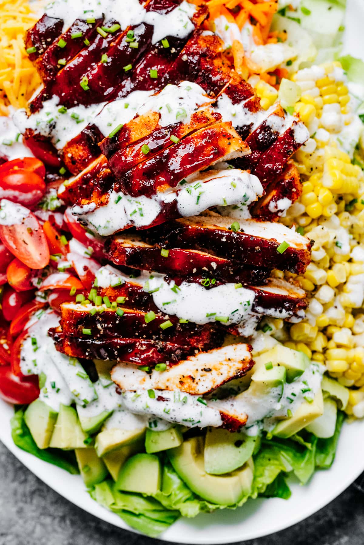 Salad greens, sliced chicken, tomatoes, diced avocados, corn, and cheeses are arranged on an oval serving platter, all drizzled with a creamy dressing over the top.