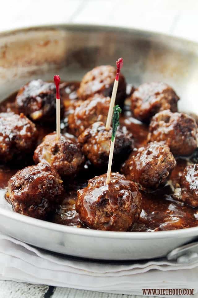 Close up of appetizer meatballs in a frying pan covered in a glaze and toothpicks sticking in them