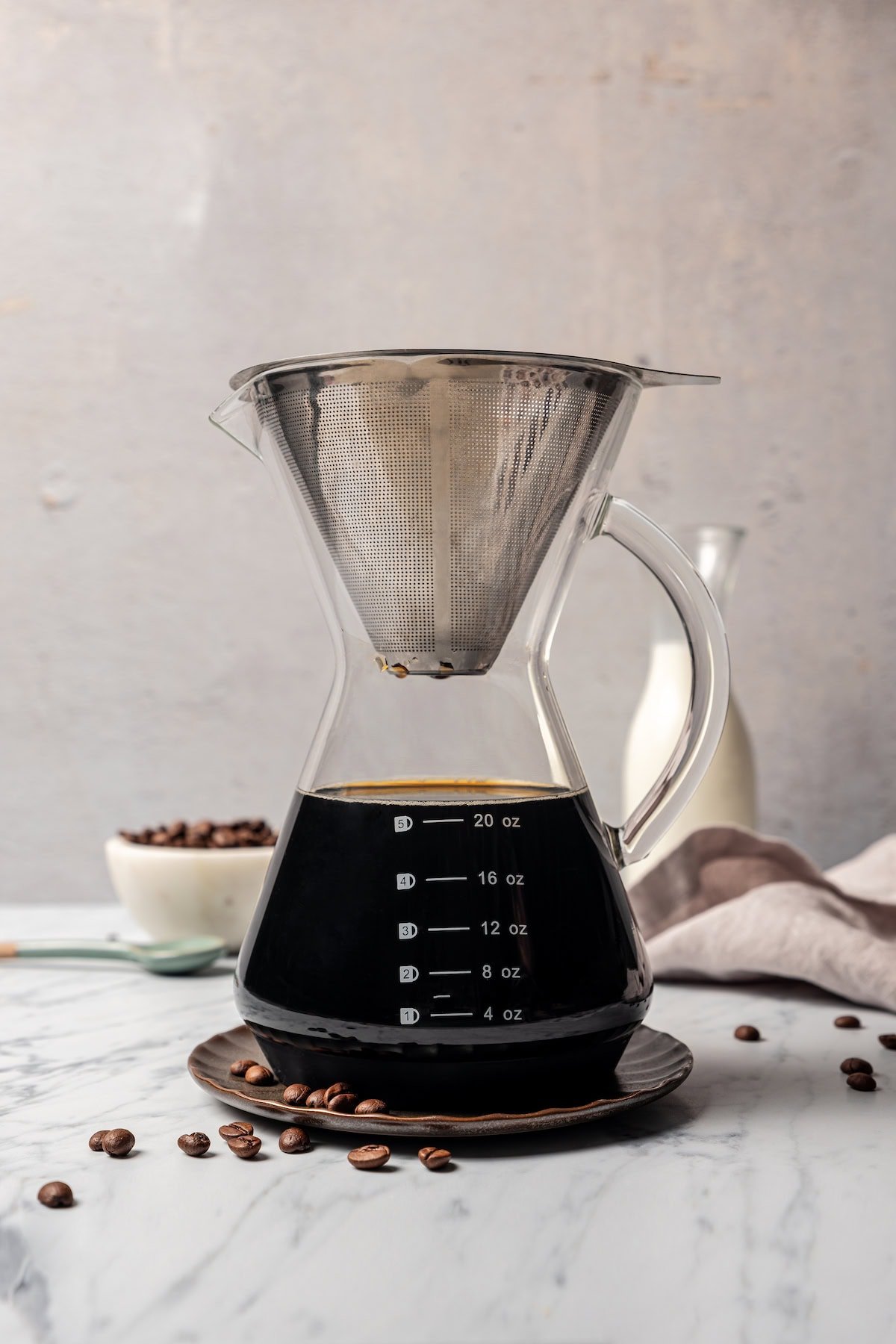 A pour over coffee maker filled with brewed coffee on a countertop next to scattered coffee beans.