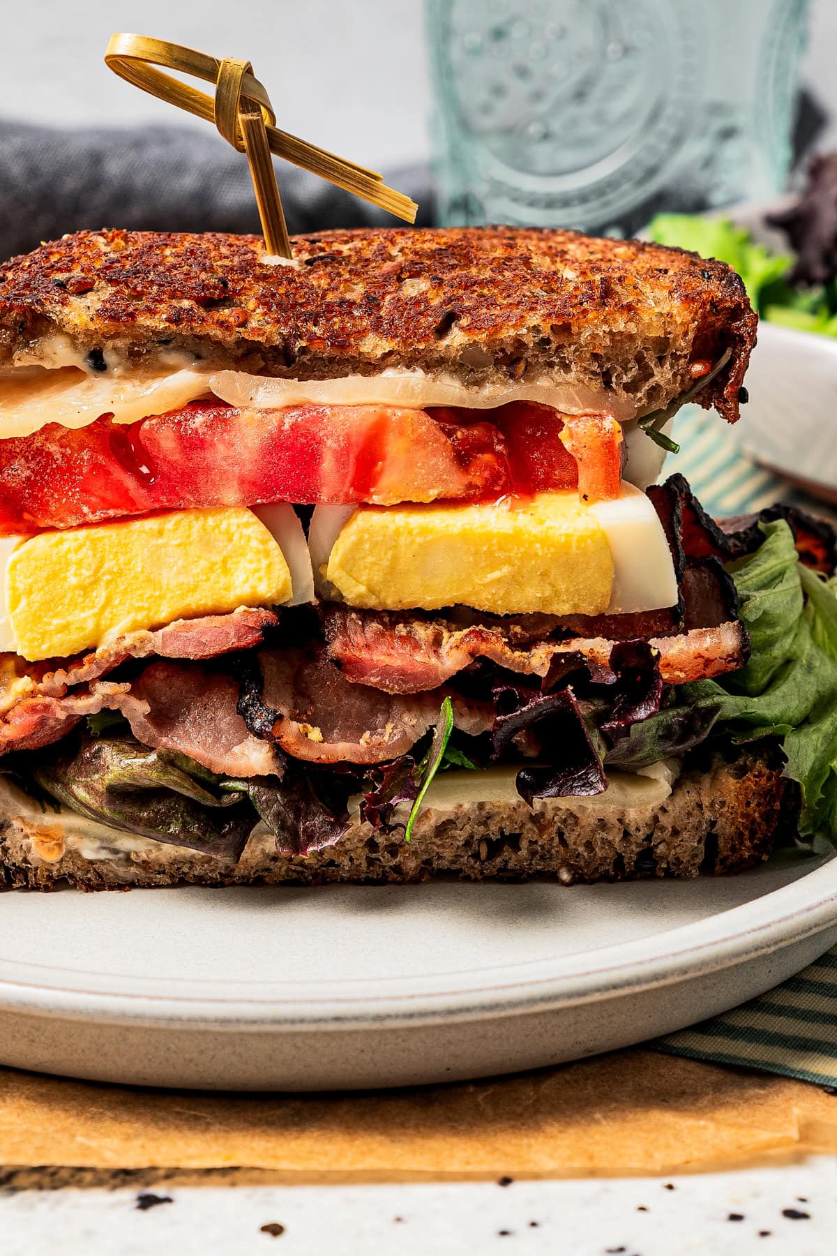 Close-up image of a grilled cheese sandwich with tomatoes, eggs, and bacon.