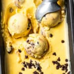 An ice cream scoop resting in a tub of chocolate chip cookie dough ice cream.