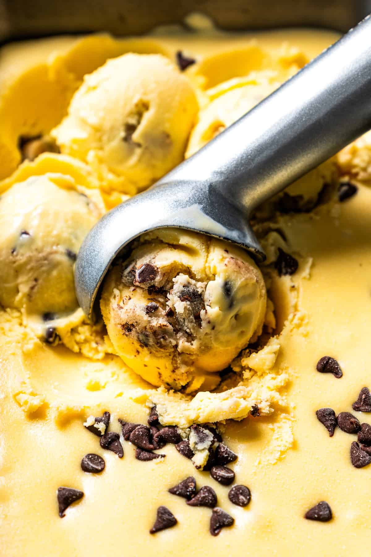 This chocolate chip cookie dough ice cream combines creamy homemade vanilla ice cream with irresistible chunks of buttery cookie dough. Scooping out homemade chocolate chip cookie dough ice cream from a tub.