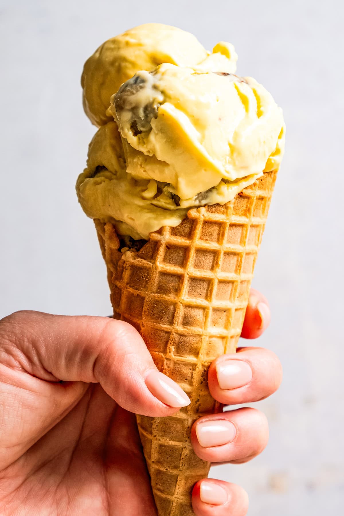 This chocolate chip cookie dough ice cream combines creamy homemade vanilla ice cream with irresistible chunks of buttery cookie dough. A hand holding up a cone of homemade chocolate chip cookie dough ice cream.
