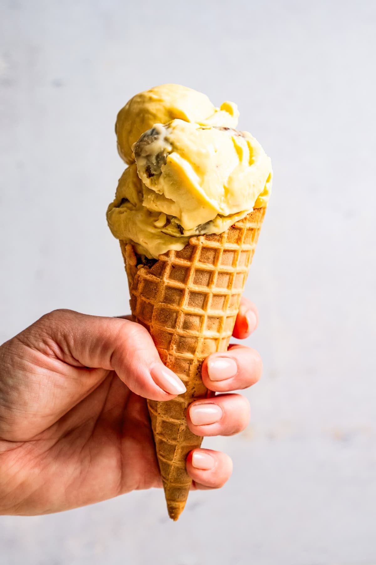 This chocolate chip cookie dough ice cream combines creamy homemade vanilla ice cream with irresistible chunks of buttery cookie dough. A hand holding up a cone of homemade chocolate chip cookie dough ice cream by diethood.