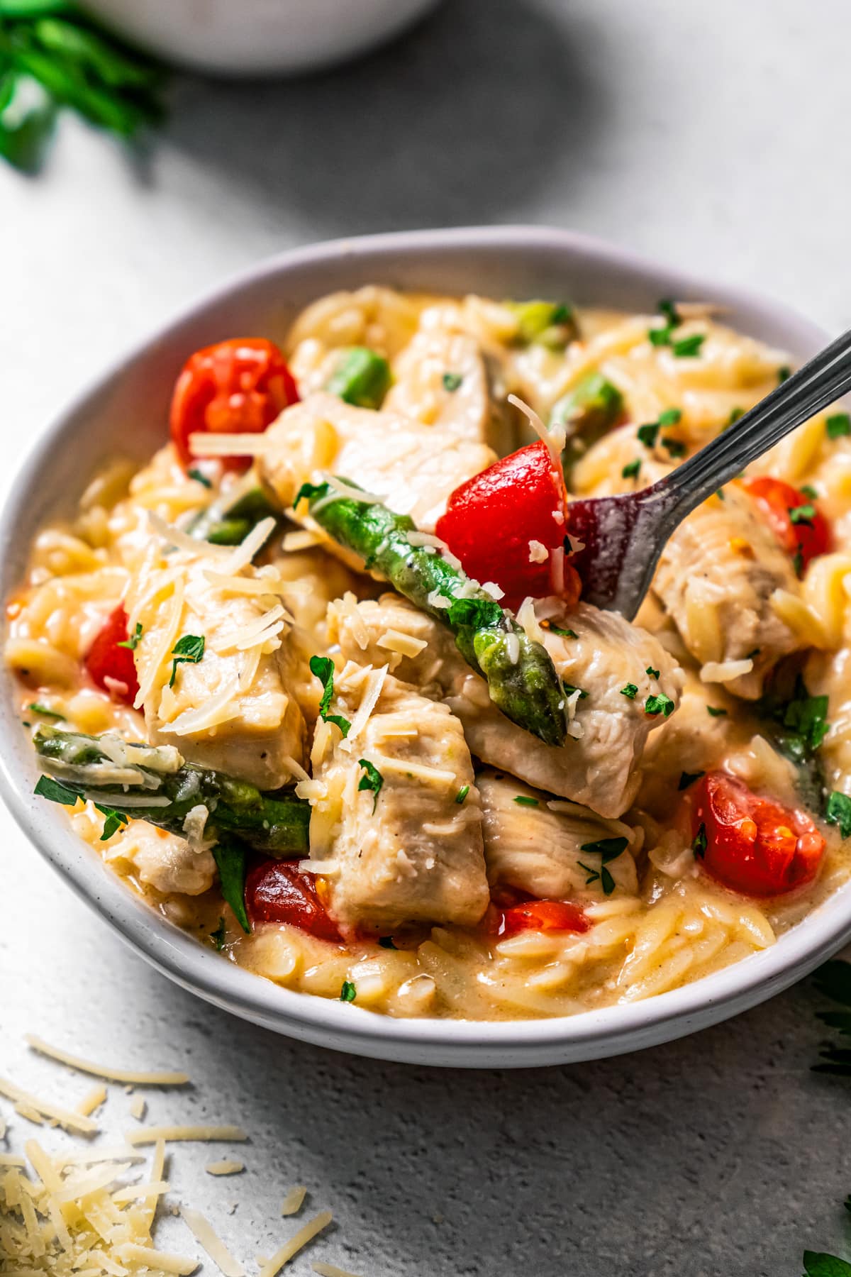 Side overhead view of a bowl of creamy chicken orzo with asparagus and tomatoes.