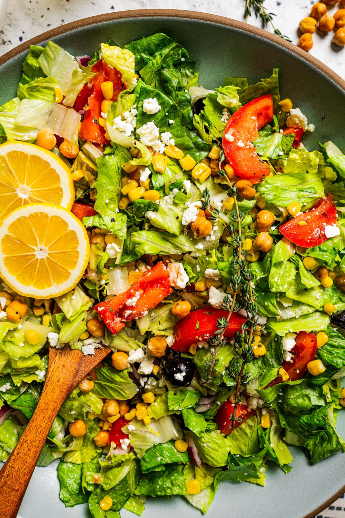 Close-up shot of a Mediterranean salad with lettuce, tomatoes, corn kernels, chickpeas, and lemon slices.