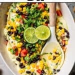 Avocado dip topped with lime wedges and fresh cilantro, served in a dish with a spoon.