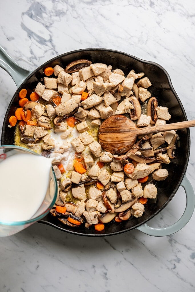 Milk added to chicken and veggies in a skillet to make a creamy pasta sauce.