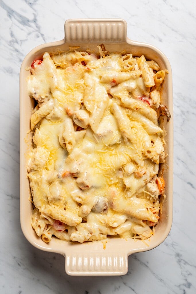 Baked chicken pasta in a casserole dish topped with melted cheese.