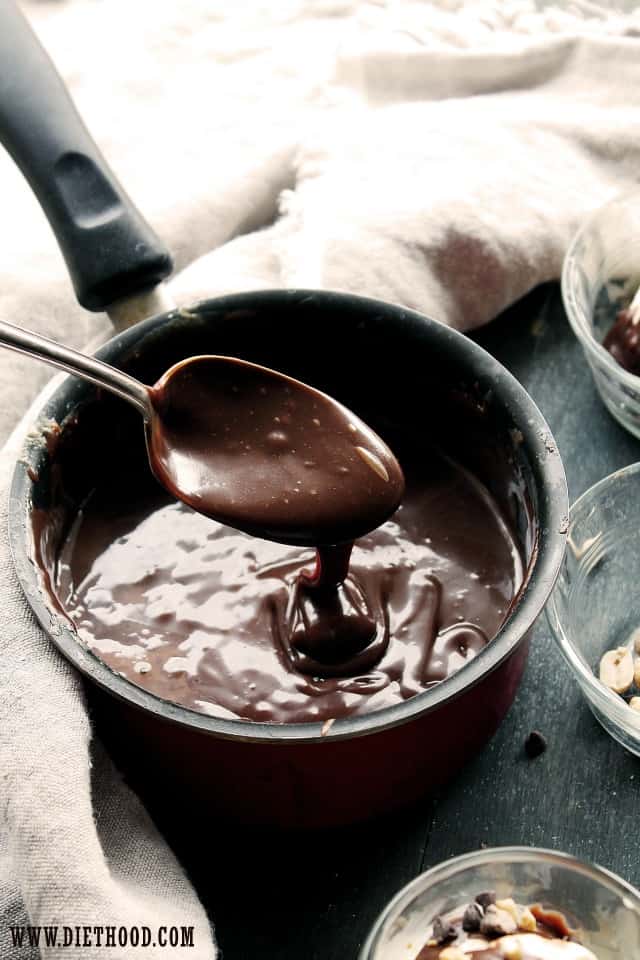 A spoon holding up homemade hot fudge sauce over a pan of more hot fudge sauce.