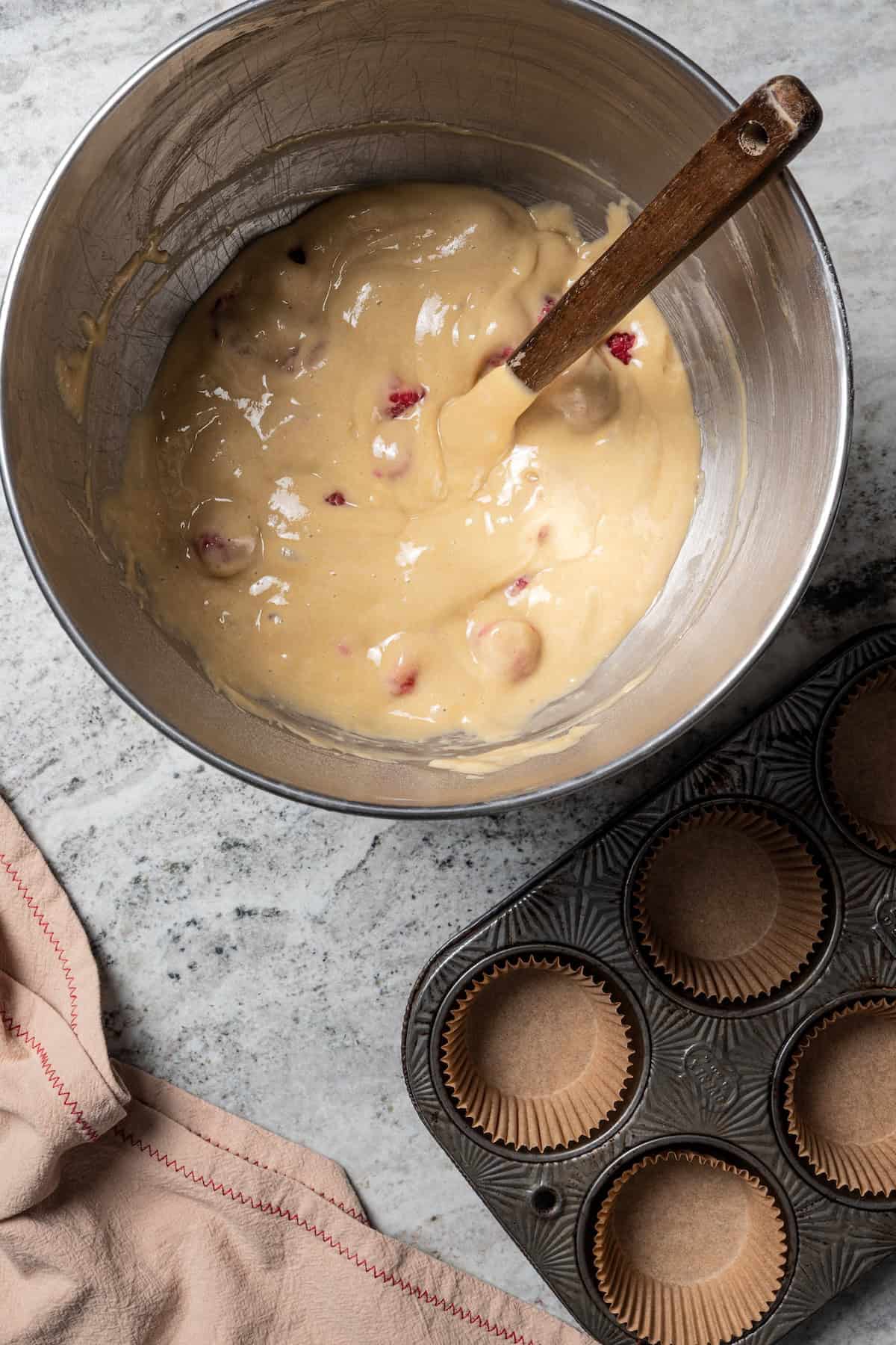 These easy raspberry muffins are fluffy and moist, made with yogurt, brown sugar, and heaps of fresh raspberries. Like summer in a muffin pan! Raspberry muffin batter in a mixing bowl next to a lined muffin pan.