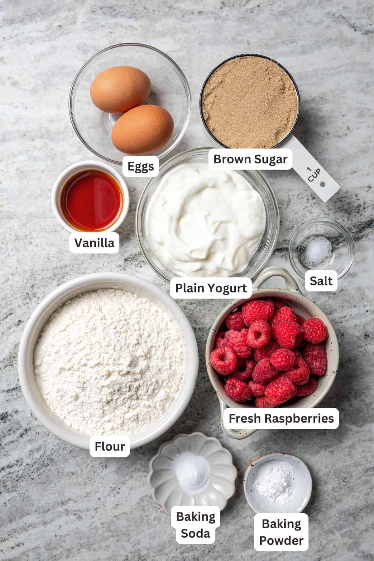 These easy raspberry muffins are fluffy and moist, made with yogurt, brown sugar, and heaps of fresh raspberries. Like summer in a muffin pan! Raspberry muffins ingredients with text labels overlaying each ingredient.