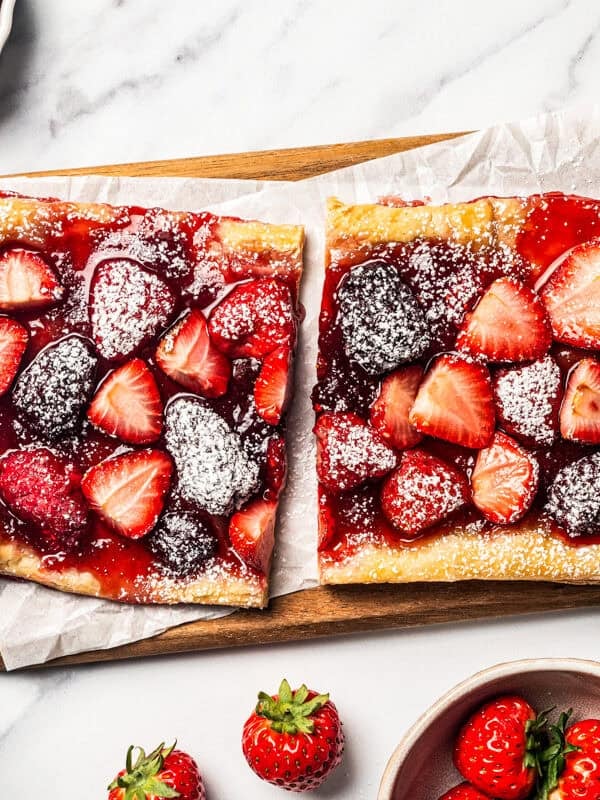 Berry tart slices are dusted with powdered sugar and arranged on a wooden cutting board.