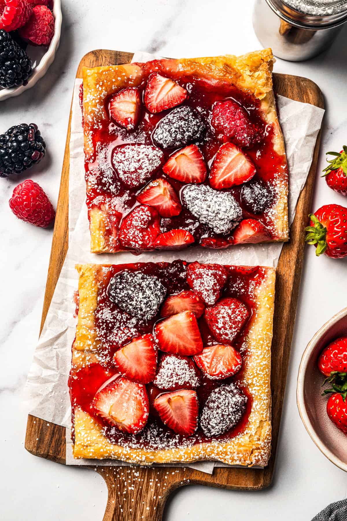 This berry tart is ready to bake in 10 minutes, with fresh berries, sweet jam, and buttery puff pastry. The perfect quick and easy dessert! Berry tart slices are dusted with powdered sugar and arranged on a wooden cutting board.