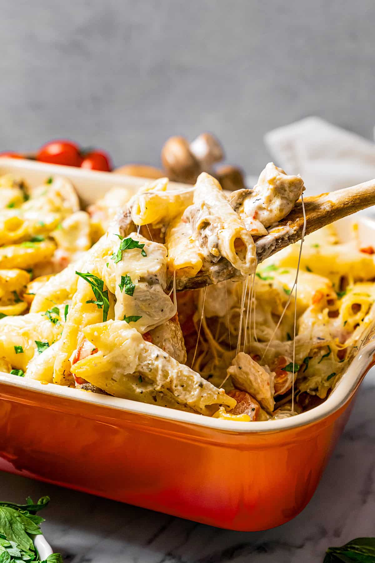 A wooden spoon lifting a scoop of chicken pasta casserole from a casserole dish.