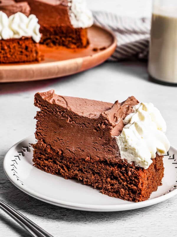 A slice of chocolate mousse cake on a plate with a chocolate mousse cake in the background.