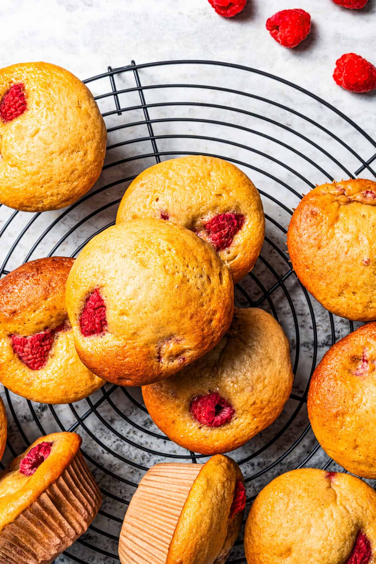 These easy raspberry muffins are fluffy and moist, made with yogurt, brown sugar, and heaps of fresh raspberries. Like summer in a muffin pan! Overhead view of assorted raspberry muffins on a round wire cooling rack.