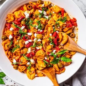 Tortellini pasta salad in a salad bowl with two wooden spoons placed in the salad.