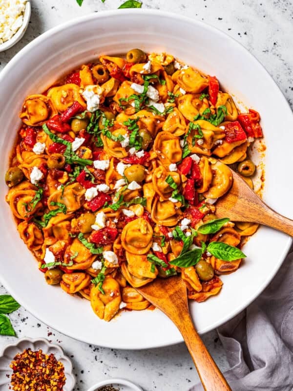 Tortellini pasta salad in a salad bowl with two wooden spoons placed in the salad.