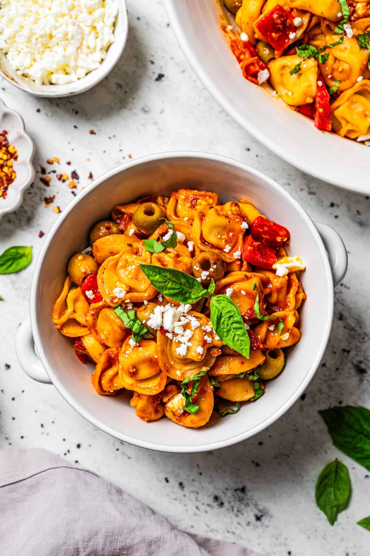 This Mediterranean tortellini pasta salad is a flavorful, easy summer side dish with cheesy tortellini, olives, red peppers, and feta cheese! Bowl of tortellini pasta salad garnished with basil leaves.