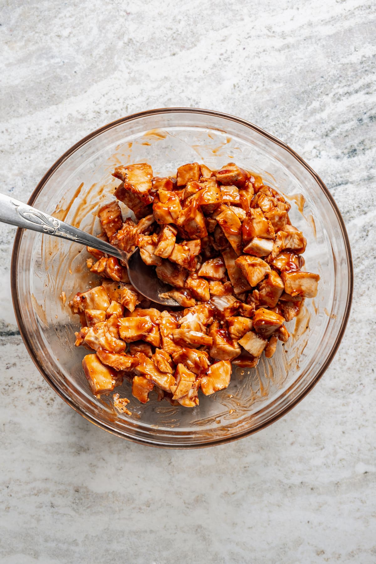 Chicken pieces tossed with BBQ sauce in a glass bowl.