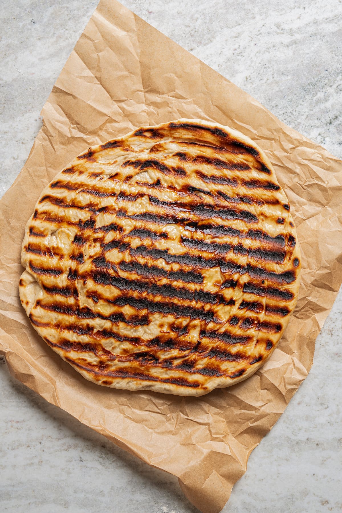 Grilled pizza crust on a piece of parchment paper.