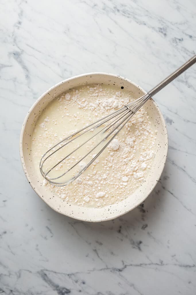 Milk, broth, and flour in a mixing bowl, with a whisk