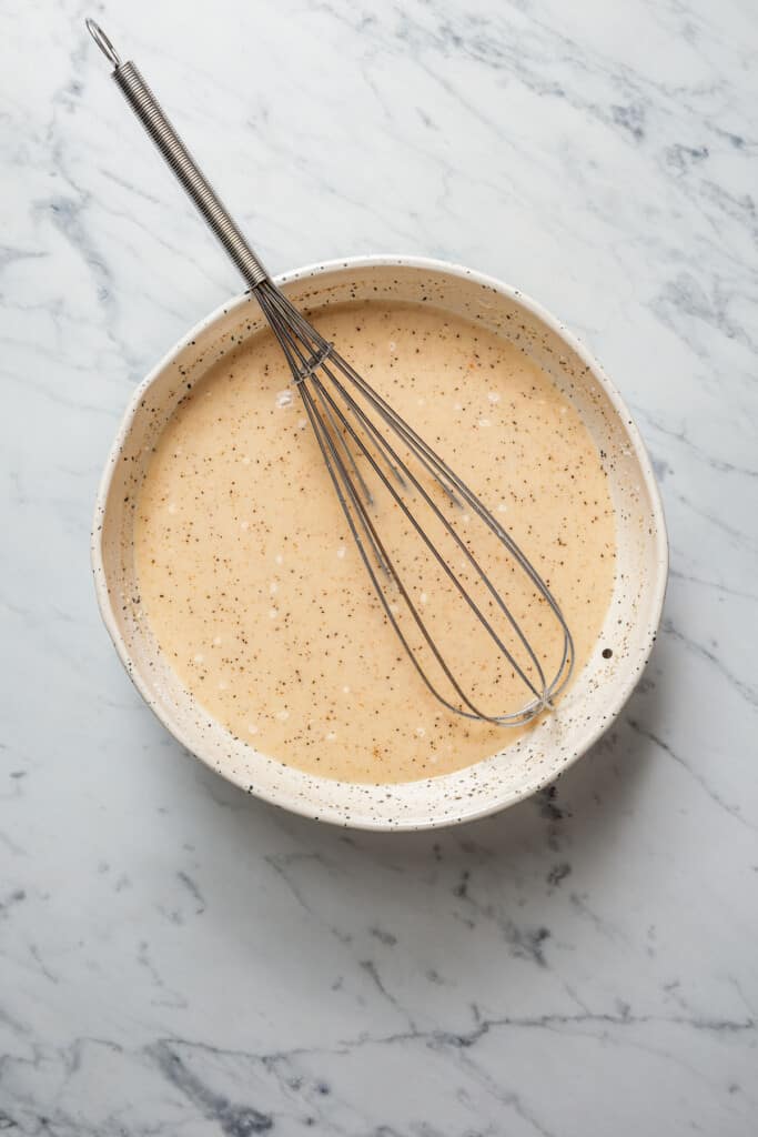 A seasoned milk and broth sauce in a mixing bowl, with a whisk