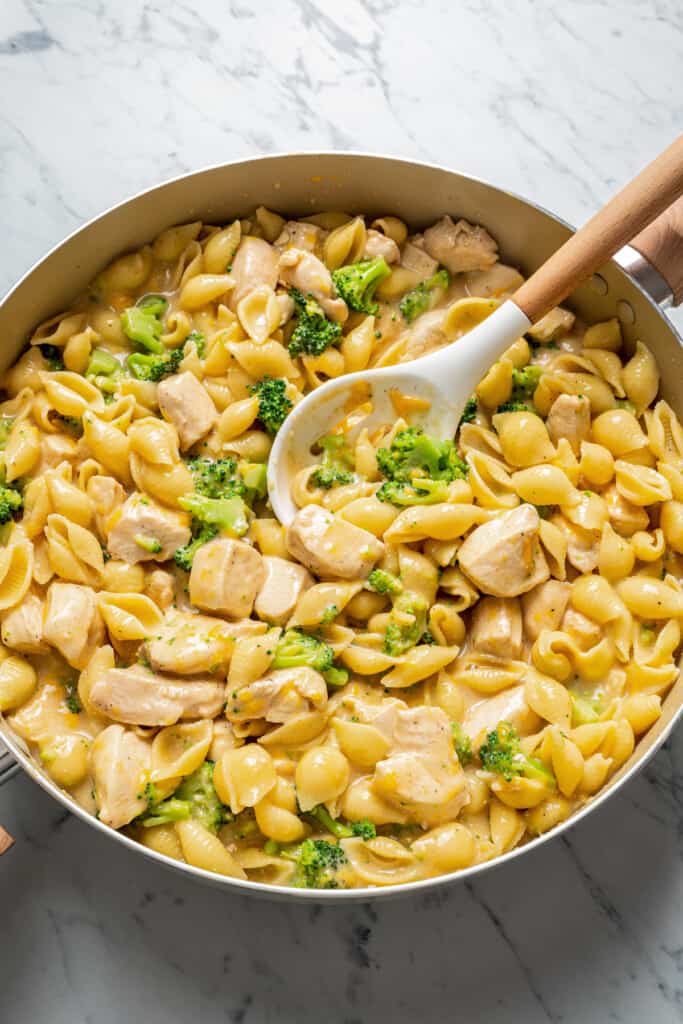 A large skillet full of chicken and broccoli pasta with a slotted spoon