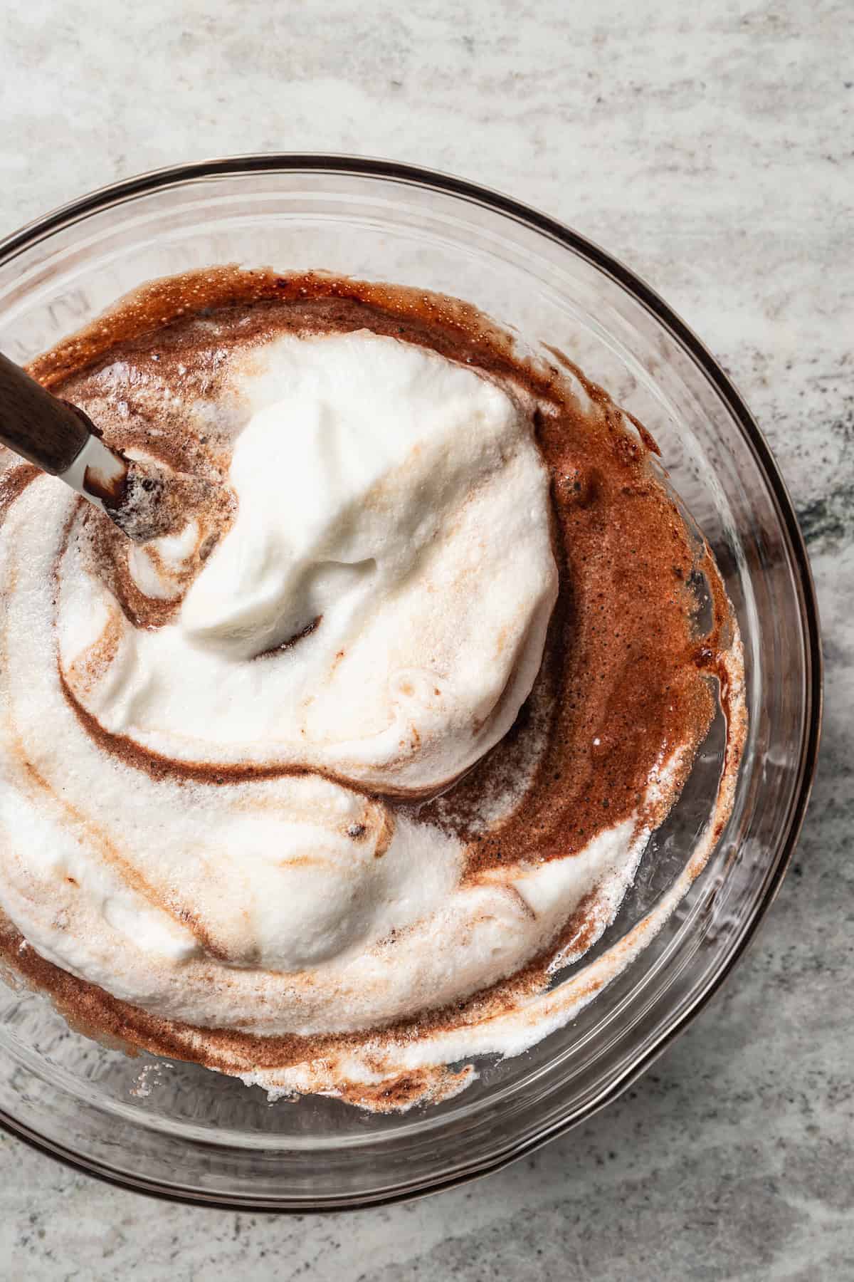 Melted chocolate mixture partially folded together with whipped egg whites in a glass bowl with a spoon.