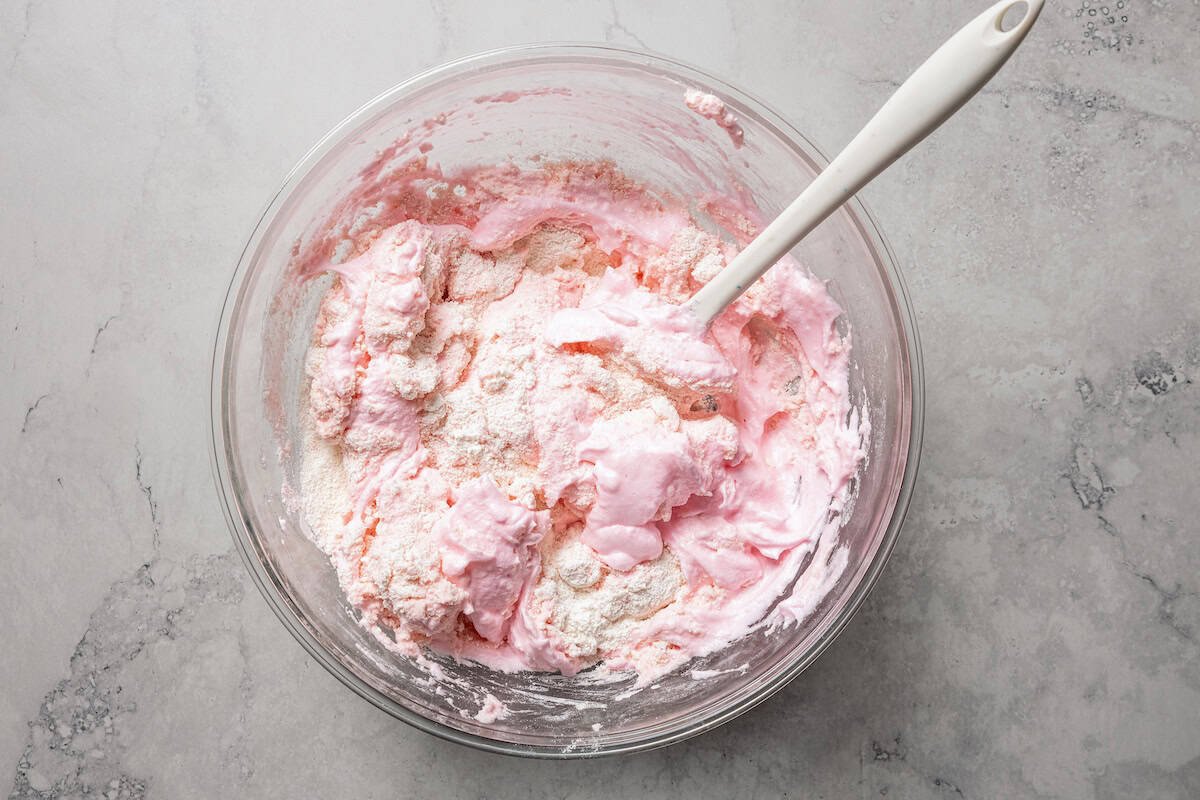 Partially mixed pink meringue in a bowl with a spoon.