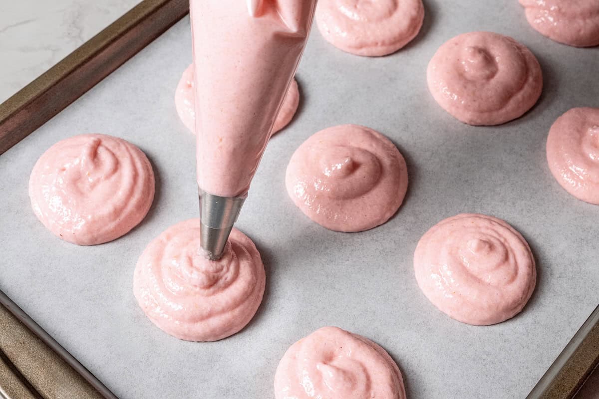 Piping pink meringue onto a baking sheet.