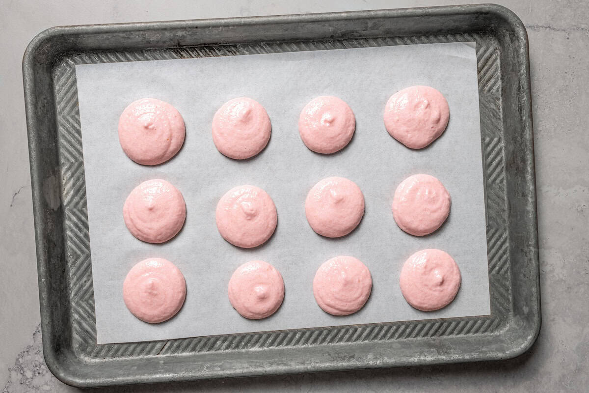 Pink meringue piped onto a baking sheet to make French macaron shells.