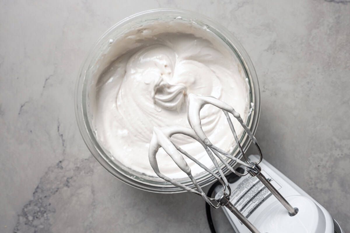 Whipped marshmallow frosting in a bowl underneath a mixer.