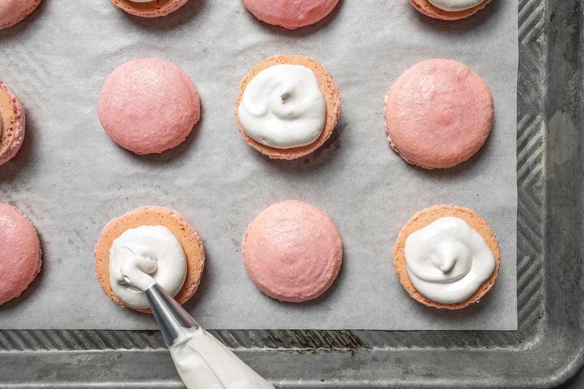 Piping marshmallow frosting onto the bottom meringue shells.