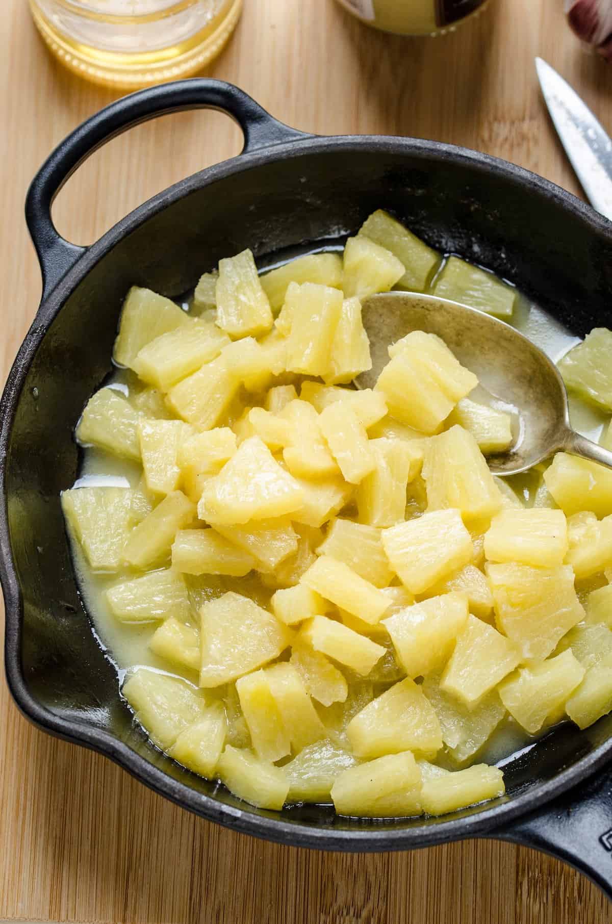 Chunks of pineapple are cooked in a skillet with melted butter.