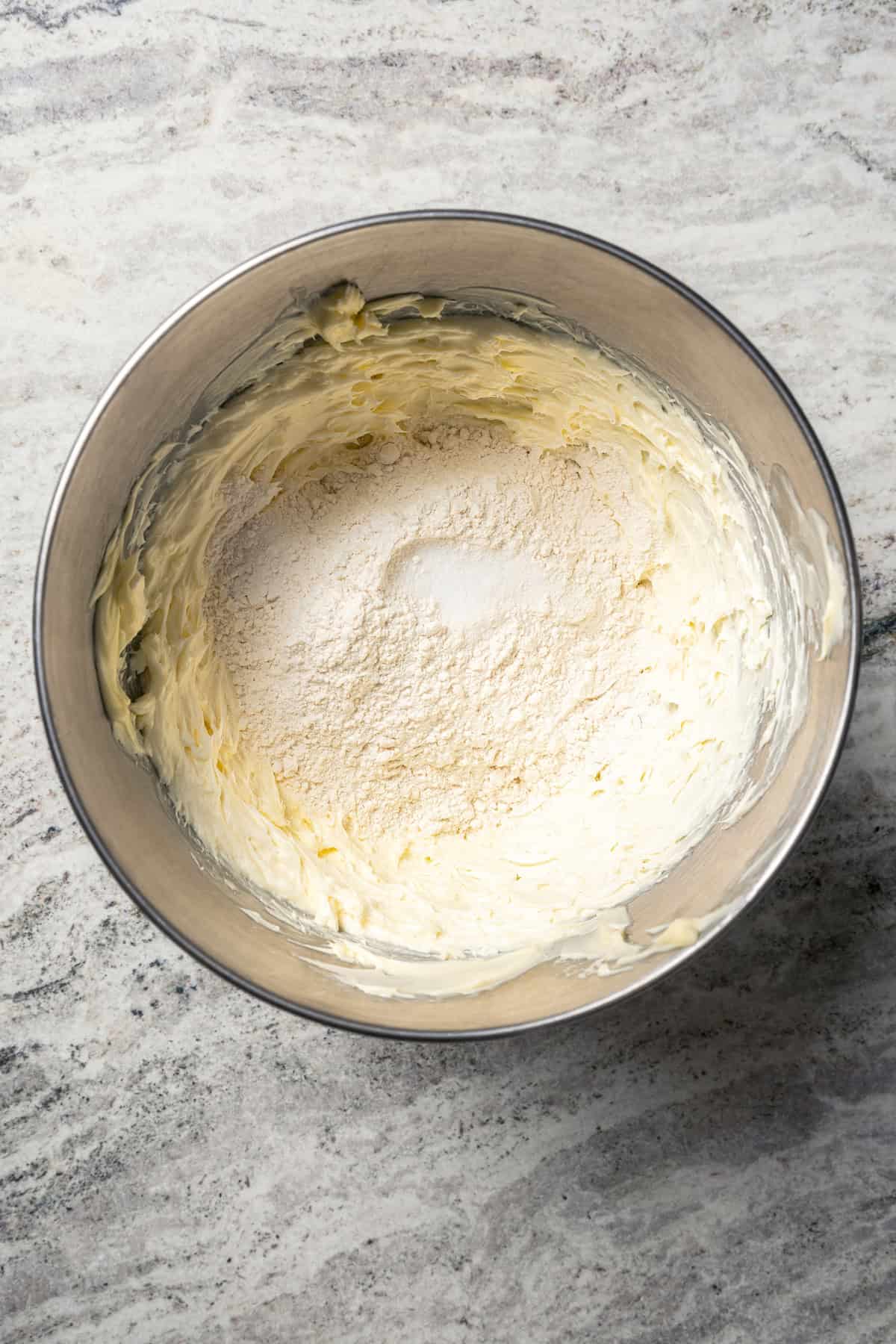 Dry ingredients added to creamed butter and cream cheese in a metal mixing bowl.