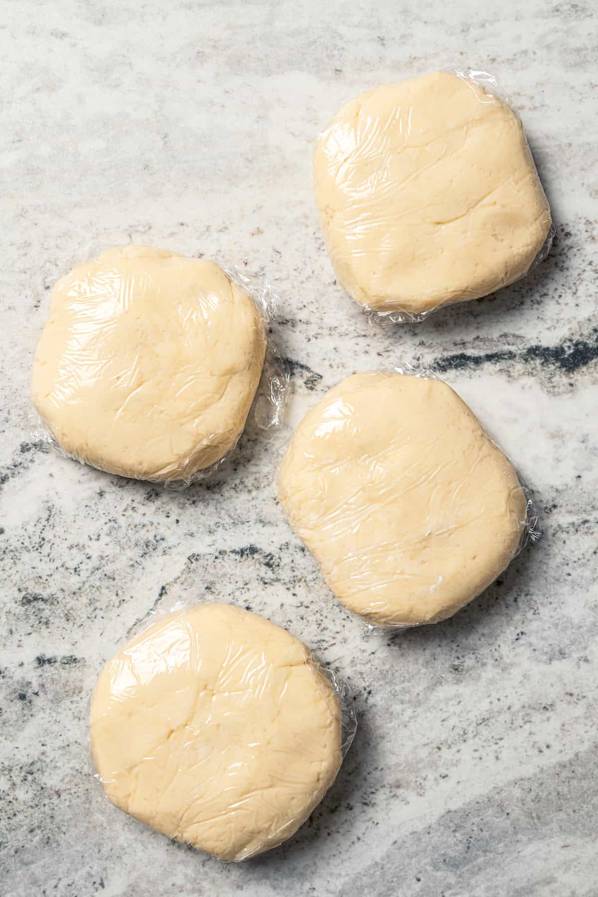 Four portions of kolacky pastry dough on a marble countertop.