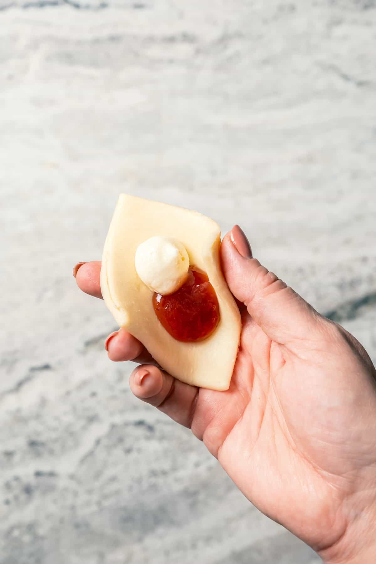 A hand holding a flat square of kolacky dough topped with strawberry and cream cheese filling.