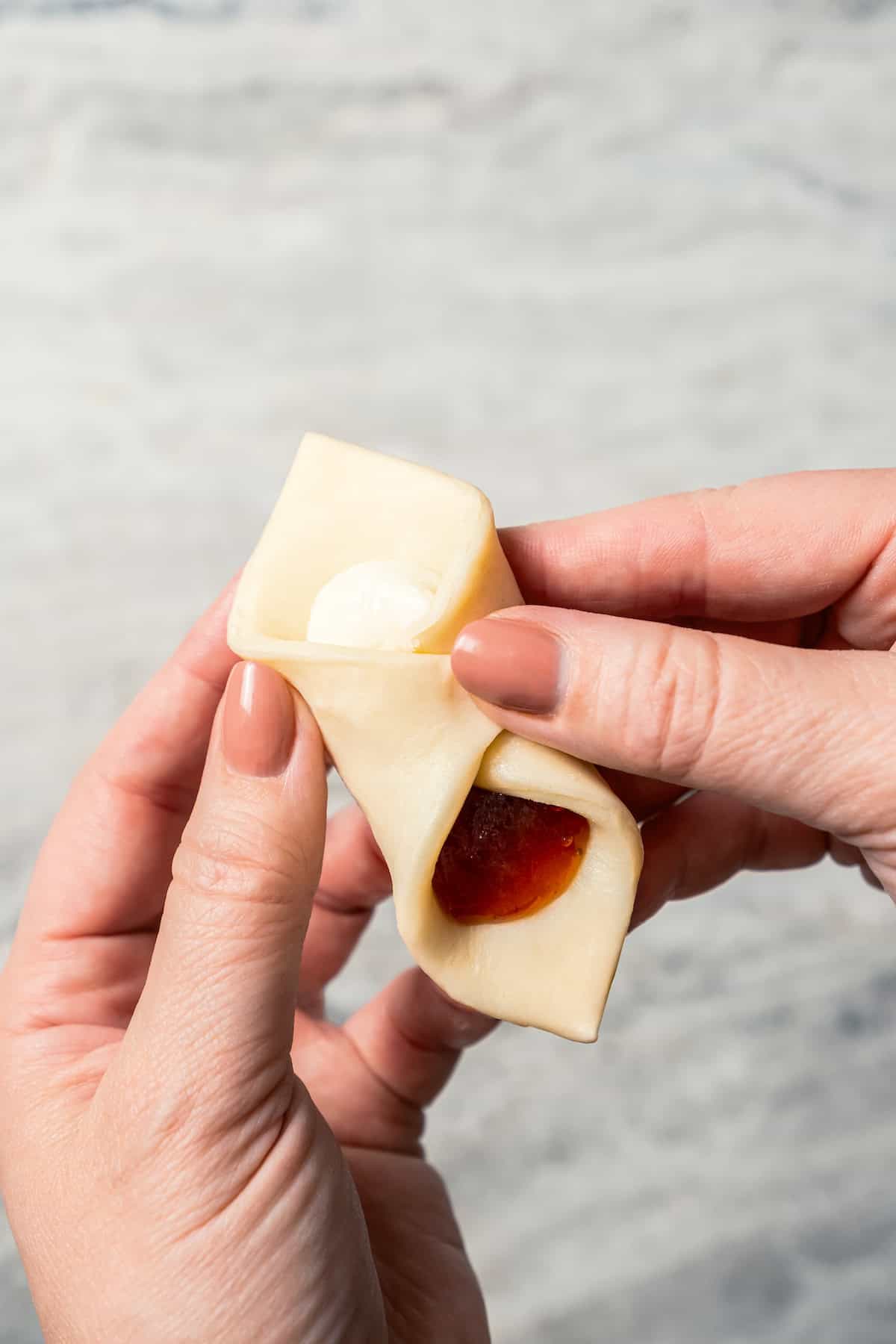 Two hands folding a square of pastry dough over strawberry and cream cheese filling.