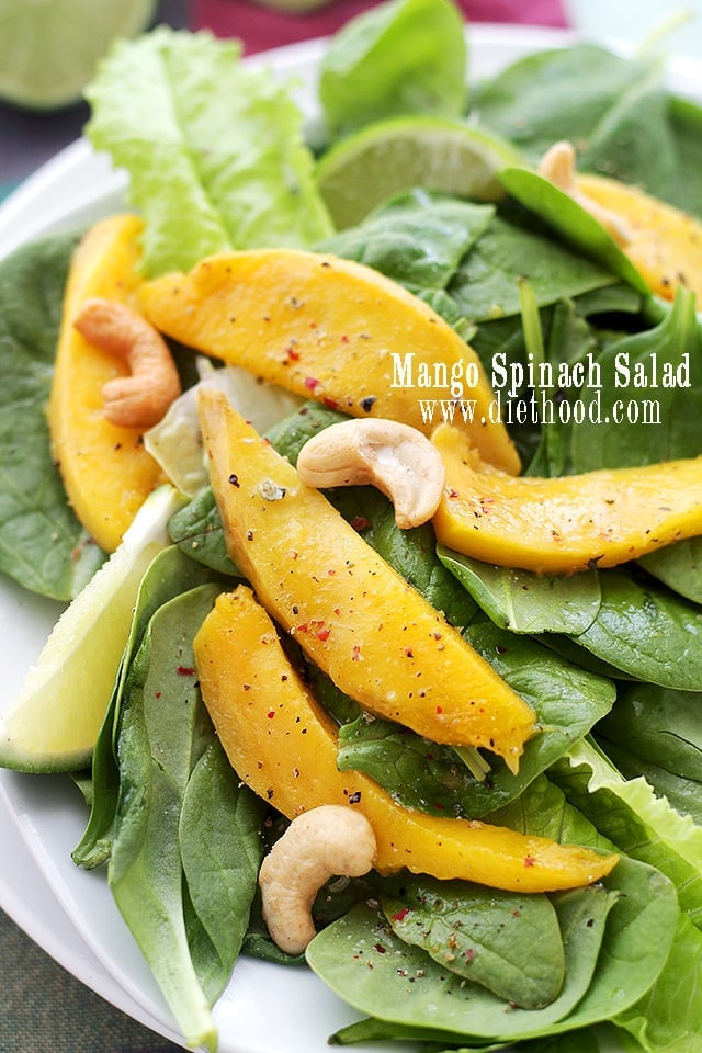 Spinach salad served on a plate with mangoes and cashews.