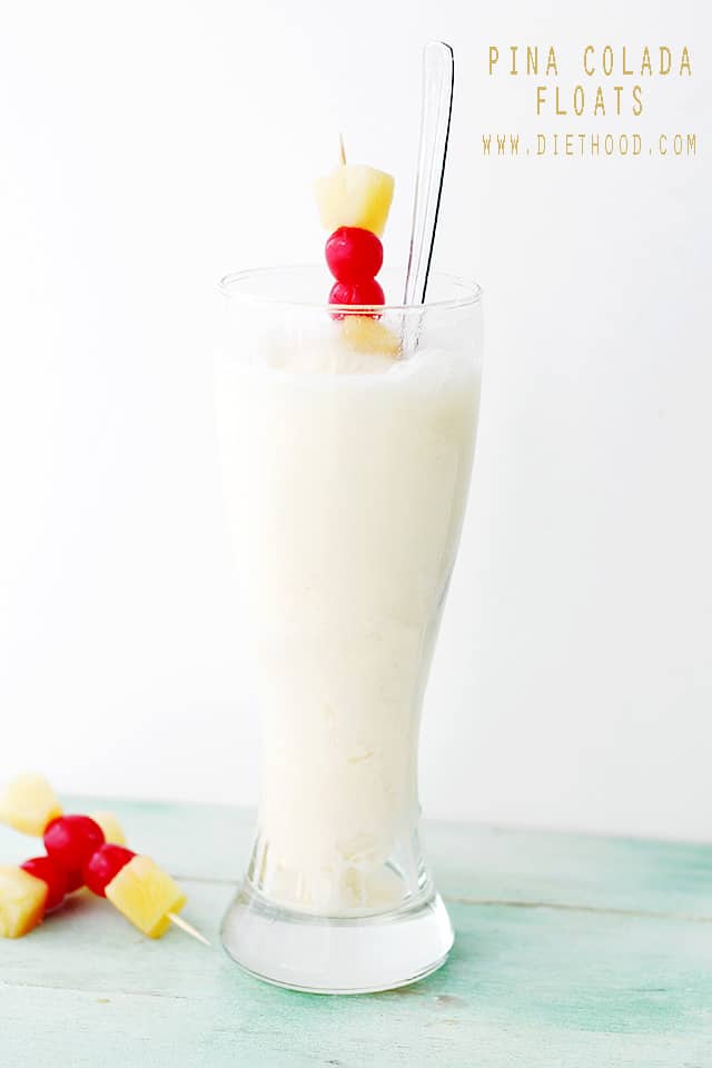 A frozen Pina Colada Float in a tall glass with pineapple, cherries and a spoon