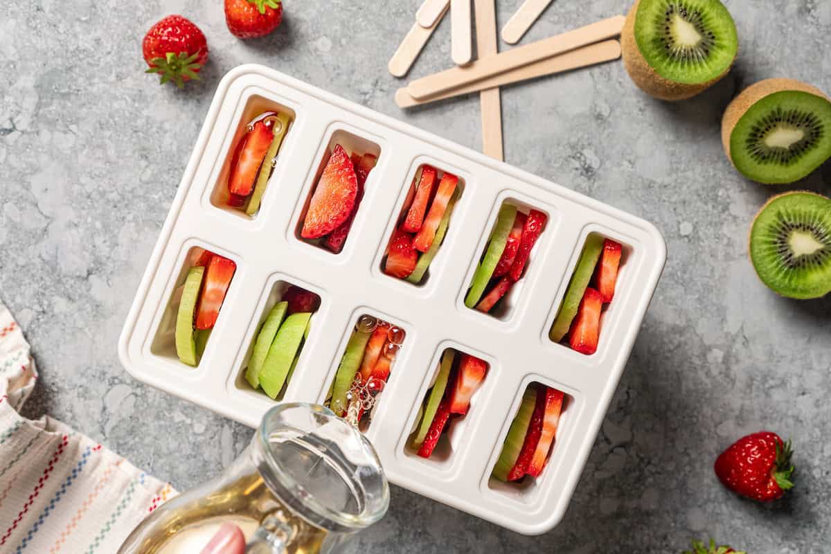 Pouring fruit juice over fresh fruit slices inside popsicle molds.
